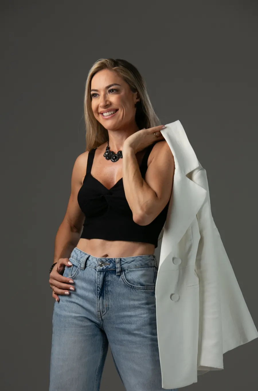 Tati de blazer branco, em pé, em um estúdio de fundo escuro