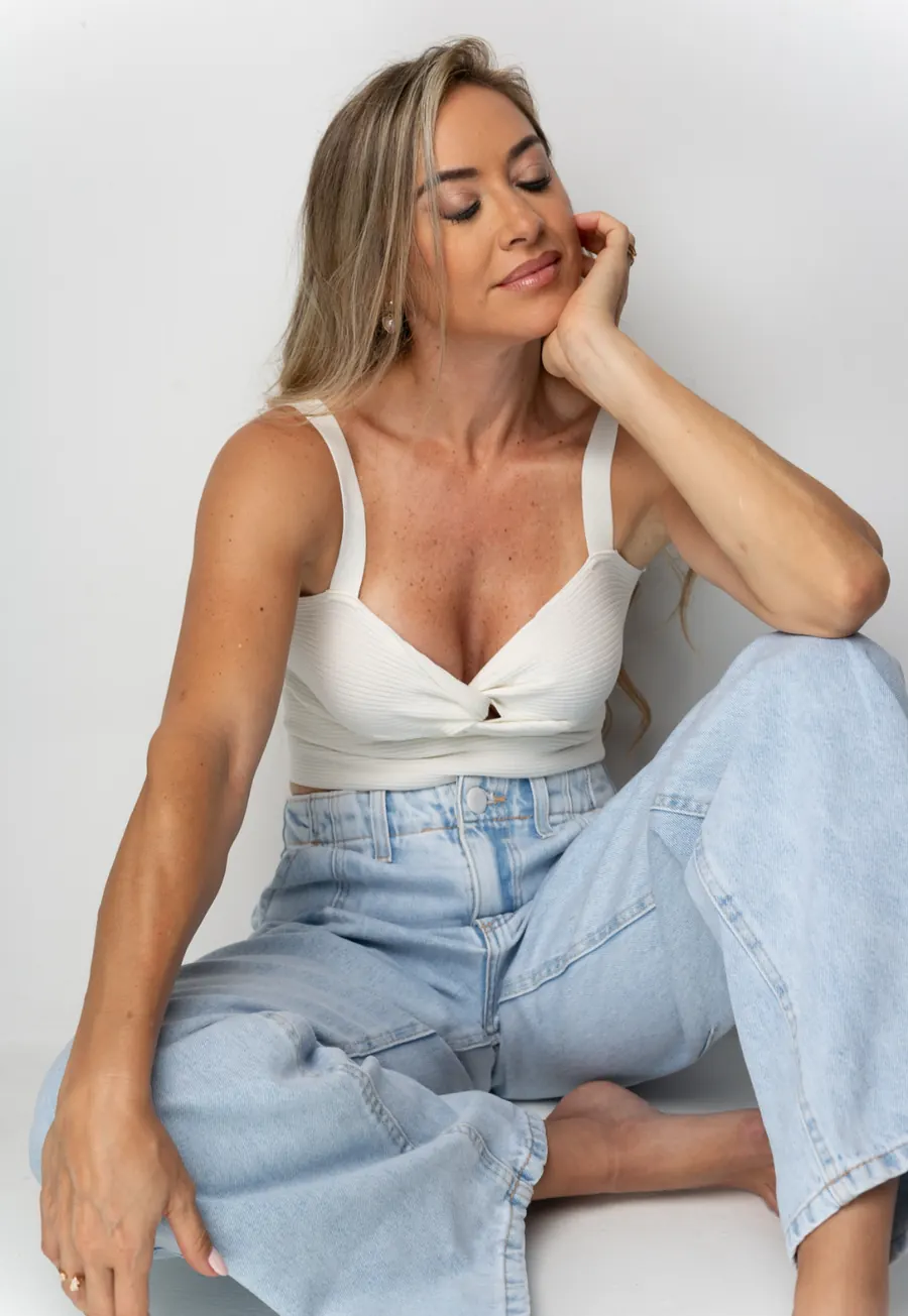 Tati sentada, apoiada na mão, em fundo claro